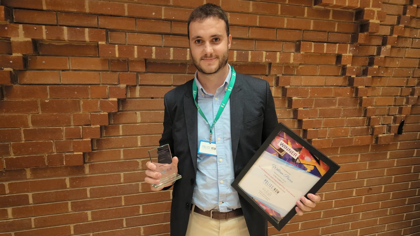 PC William Pearce holding his trophy and framed winner's certificate against a brick wall