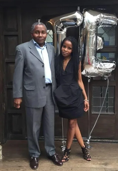 Dineo standing with her father Johnny in a doorway beside silver balloons